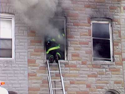 (13) A firefighter performs vent-enter-search in the front bedroom of a two-story middle-of-the-group row home. It's critical to read the smoke and heat conditions while making entry and to immediately attempt to close the door of the room. (Photo by author.)