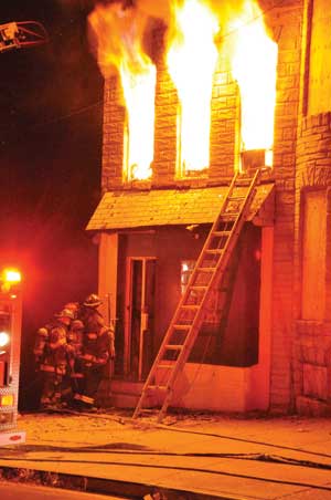 (2) Firefighters complete forcible entry, place a portable ladder, and prepare to make entry to conduct an interior search. (Photo by Nick Eid.)