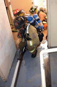 Firefighters fully flow the two-inch hoseline into a stairwell on the floor below the fire to judge the quality of its stream and to accurately read flow pressure on the in-line gauge. 