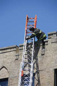 (36) The firefighter is removing a mounted attic ladder from the tip of the aerial for use on the roof.