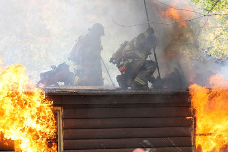 Roof firefighters with flames all around them.