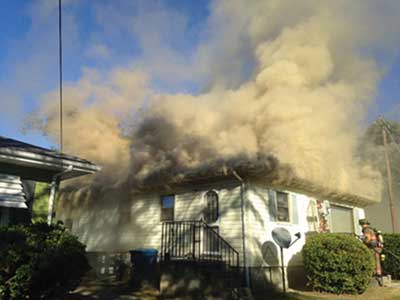 (1) Note the smoke exiting the building from the soffit area of the structure and minimal smoke exiting from where the firefighters are entering