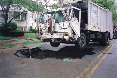 To remove the truck, a crane lifted the front of the truck while a tow truck stabilized the rear to keep it from being pulled into the hole by the crane. The hoseline maintains the water level above the shut-off water main to prevent contaminants on the water's surface from back-flowing into the water supply.