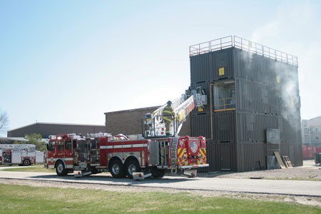 (2) In a multicompany live fire evolution, a tower ladder from one department is used for upper-level access while different fire departments advance hoselines on the interior.