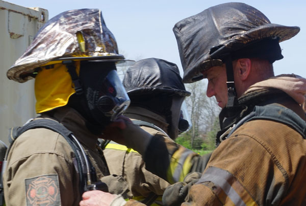 A firefighter helps adjust a comrade's gear.