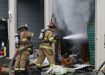 (9) When cutting or opening the overhead door, stay to the side and have a charged hoseline ready. When operating a hoseline, be prepared for the possibility of a violent flashover or the explosion of unknown contents. [Photo courtesy of the Spokane (WA) Fire Department.]