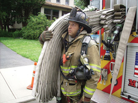 <b>(12) </b>The nozzle firefighter shoulders the 150-foot 1¾-inch preconnected minuteman load and advances it forward enough so the driver/engineer can shoulder the remaining 100 feet of flat-loaded hose and disconnect the line from the jumper (pony) line. <i>(Photo 12 by Michael Clark; photo 13 by Matt Van Ness.</i>)