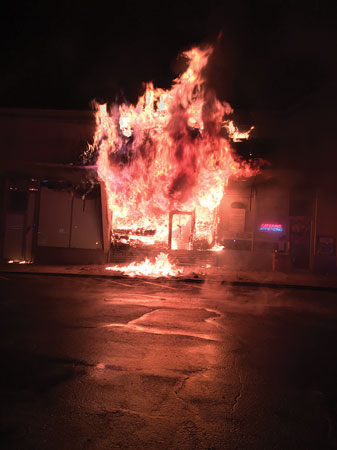 (1) A heavy volume of fire venting through the front store windows and extending into the overhanging soffit dictated a rapid fire attack with large-caliber streams and the need for extensive truck work to cut off the spread of fire. <i>(Photo by Jason Lanzilotti.)</i> 