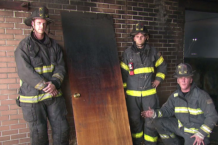 Three firefighter and a door blackened by fire