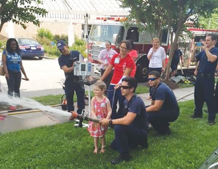 (2) Firefighter Brendan Lorson assists a small child with a little nozzle work on a visit to the local hospital.