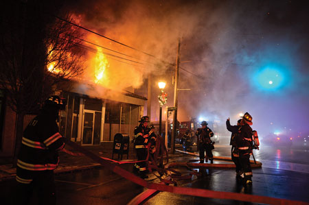 (1) Firefighters prepare to battle a fire on the second floor of a two-story commercial structure. Early in the operation, fewer firefighters are on scene but more will arrive, increasing the complexity of an emergency roll call if needed. <i>(Photos by Steve Pfost.)</i>