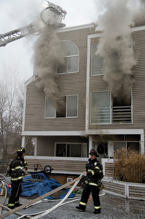 (2) Smoke is showing from the second level and at the roof level, indicating a deep-seated fire in the void spaces.