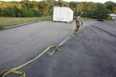 <b>(5-6)</b> The firefighter walks out holding the nozzle and coupling. As the hose unrolls, he will drop the coupling and continue to walk the nozzle to the fire.