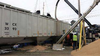 (2) Firefighters work to remove the granular fertilizer from the railcar. The lower hopper discharge chute and the mechanical fertilizer removal system are visible. (Photo by Jamie Renner.) 