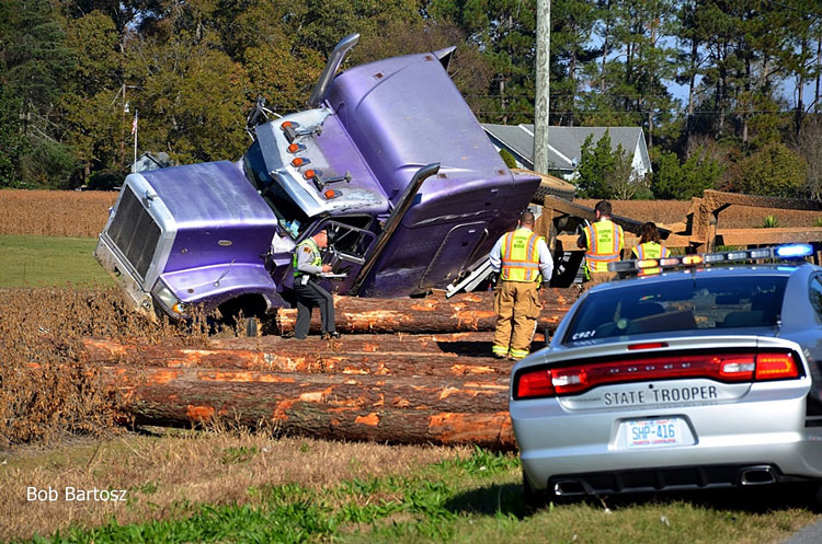 Firefighters on scene near a crashed semi with logs