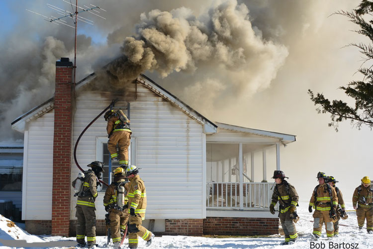 Firefighters use a hoseline on a ladder during house fire operations