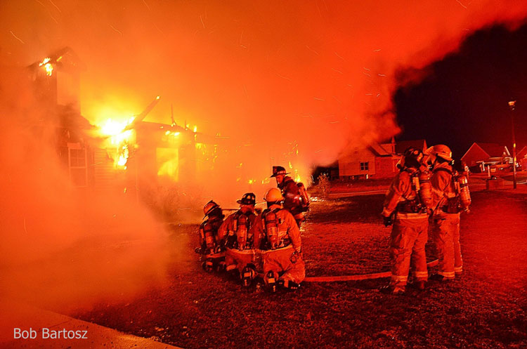 Firefighters with hoseline outside raging house fire