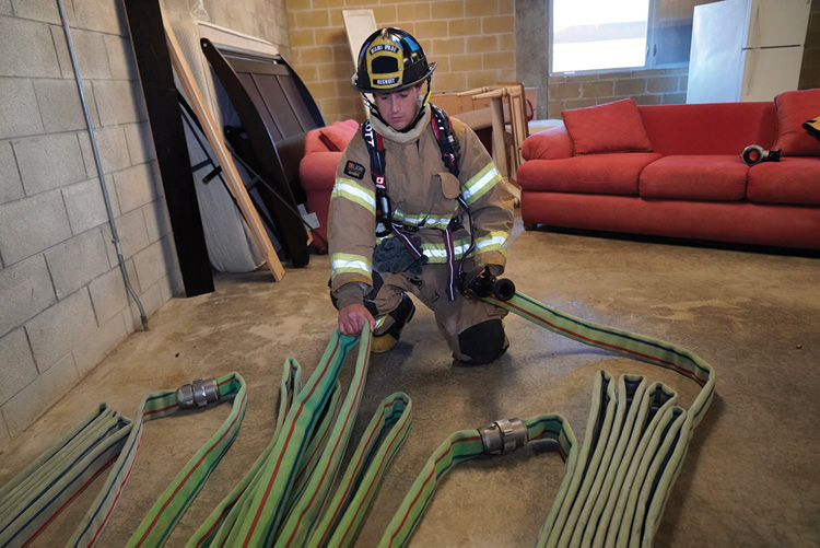 The officer secures the hose during the stretch by grasping the nozzle and the middle of the load. 