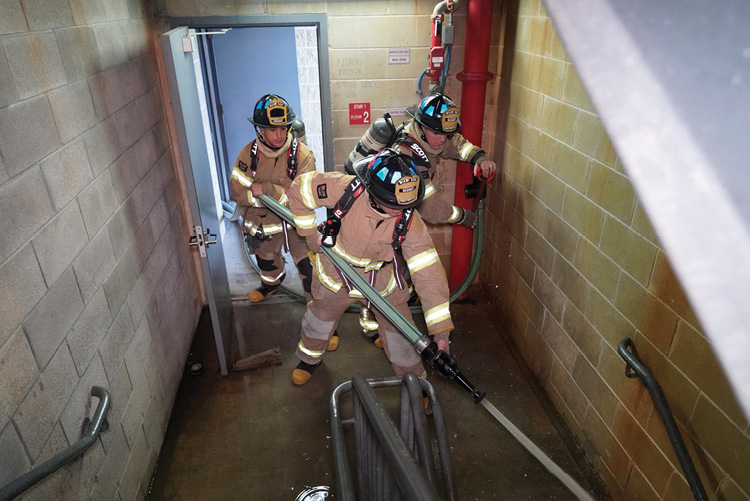 Firefighters charge the hoseline with the nozzle flowing at the standpipe outlet. The nozzle will not ascend to the fire floor before the nozzle firefighter and the firefighter opening the outlet agree on the pressure and the quality of the stream. 