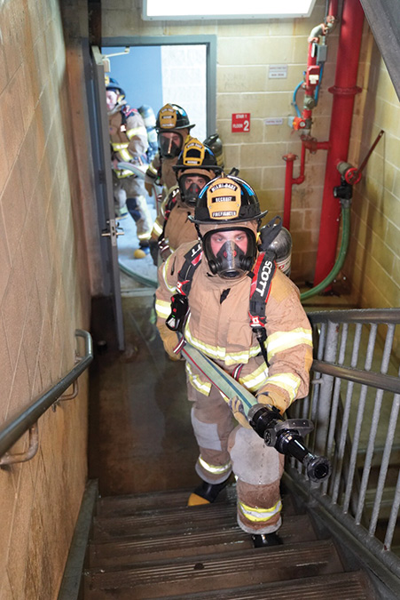 The nozzle team ascends the stairs to the fire floor with a charged hoseline.