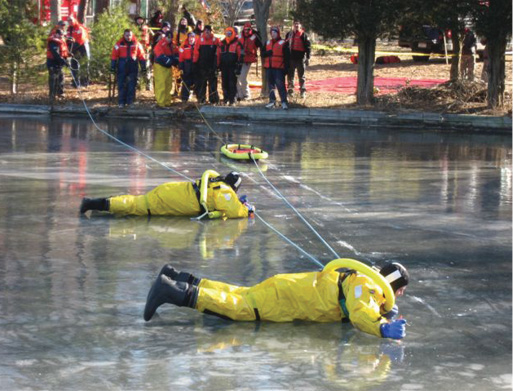 Surface ice rescue tech 2 (right) pretends to be fatigued and becomes a human ice screw while the shore pulls the sled to shore to pick up a fresh tech 3. In an operation, technicians could be more than 100 feet apart depending on the condition of the ice. Tech 3 is pulled to tech 2 by shore personnel. 