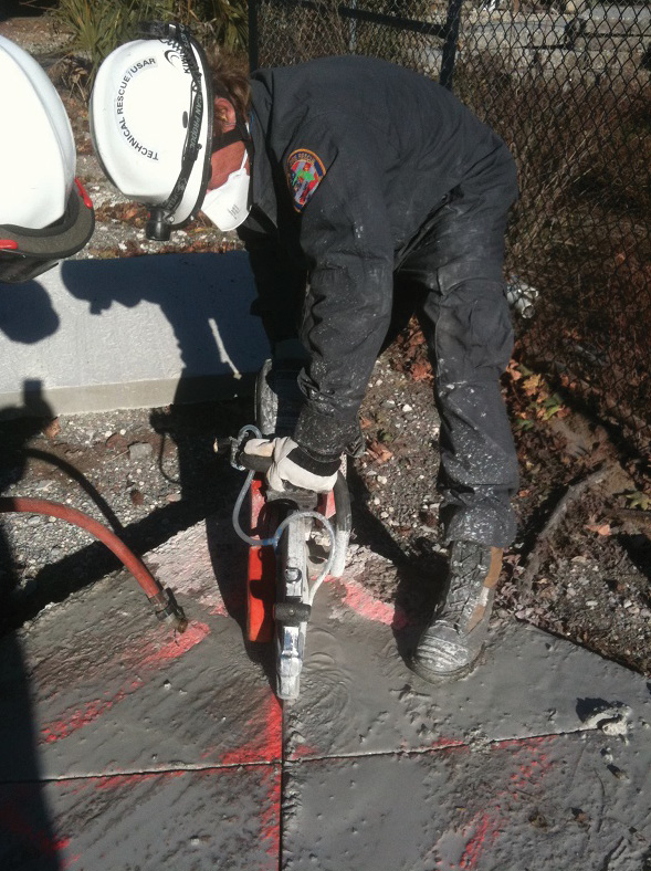 Rescuers are making an “X” cut across the entry point to weaken the concrete in a dirty breach.