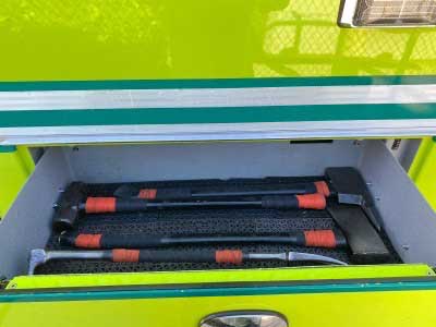 Firefighting tools including a halligan, ax, and sledgehammer inside a compartment on a fire truck