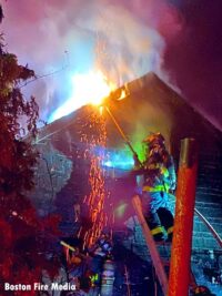 Boston firefighter on a ladder as flames vent from roof