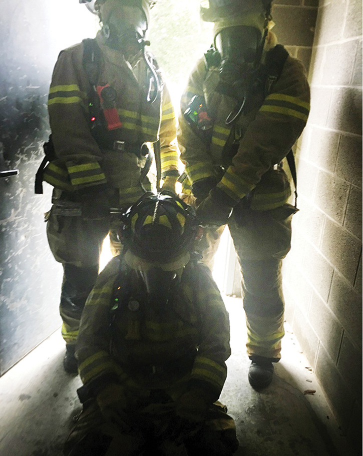 Two firefighters with a tool dragging a down firefighter down the hallway. Note the clearance issue.