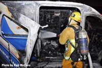 A firefighter aims a hoseline on the interior of the burned ambulance