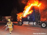 A firefighter stretches a hoseline in front of a burning tractor trailer