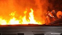 A firefighter on the roof with flames shooting through it