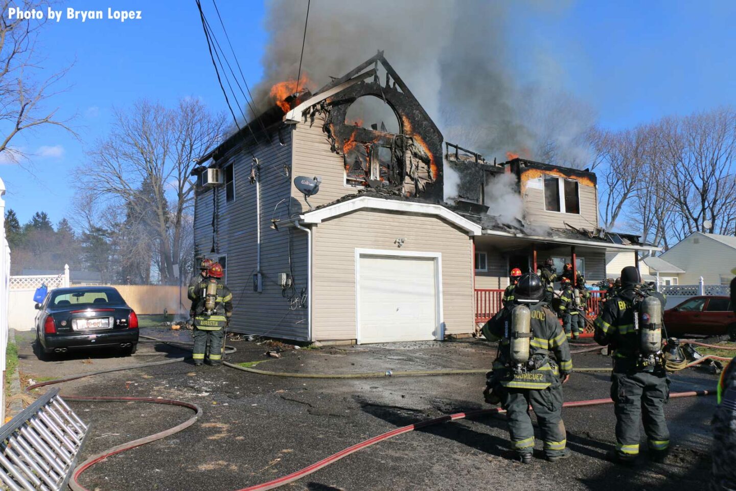 Another view of the home, with flames visible and firefighters at work