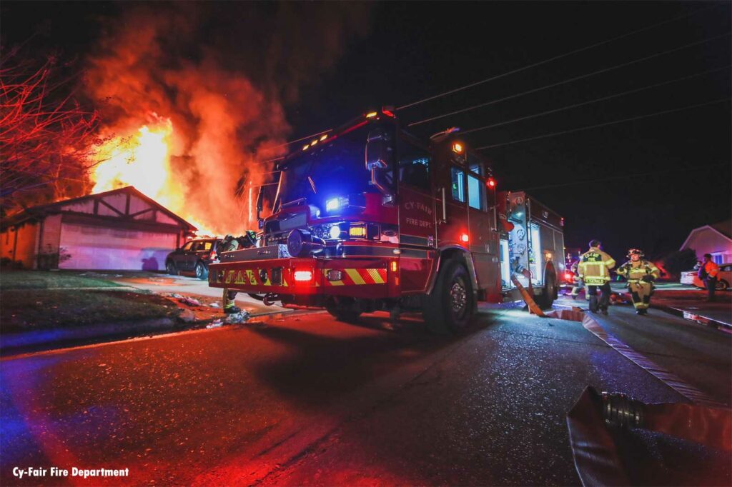 Cy-Fair fire apparatus with flames from house fire in the background