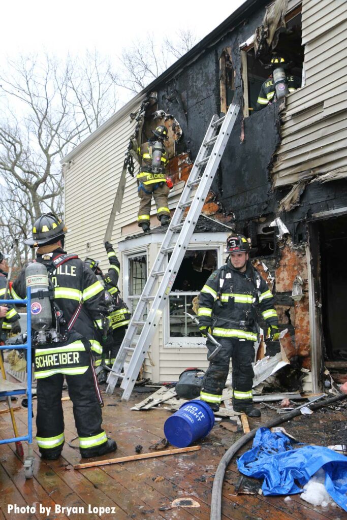 Firefighters operating at a house fire scene in Long Island with ground ladders thrown