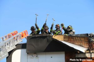 FDNY members wielding hooks and irons on the roof of a building in Queens