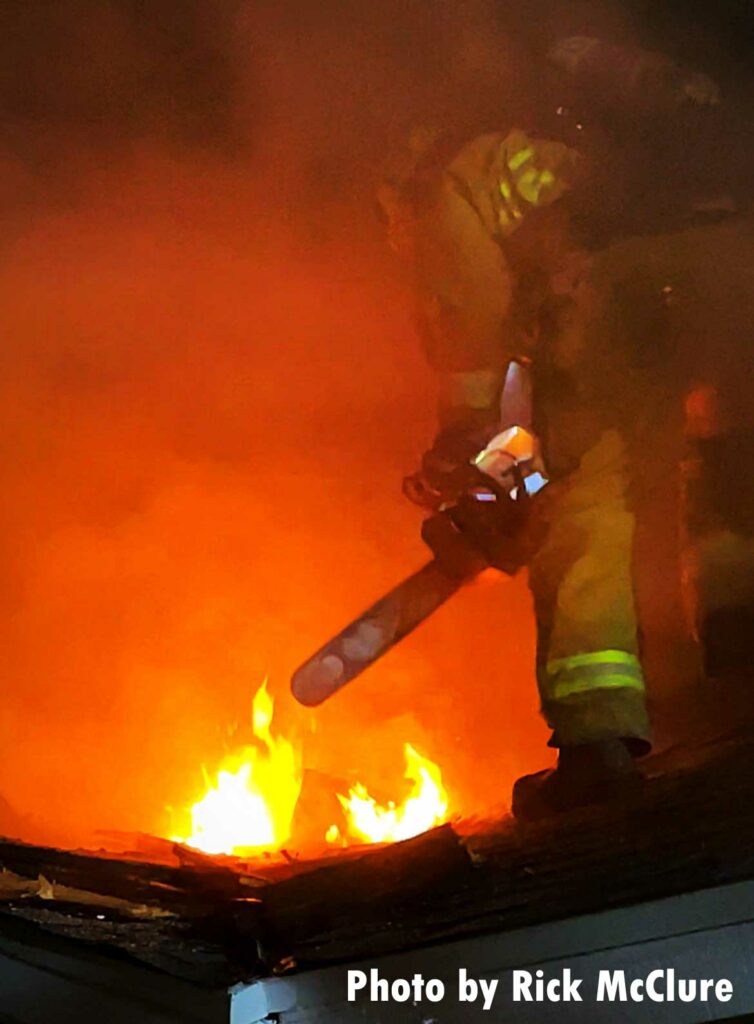 Firefighter with a chainsaw on the roof with flames showing