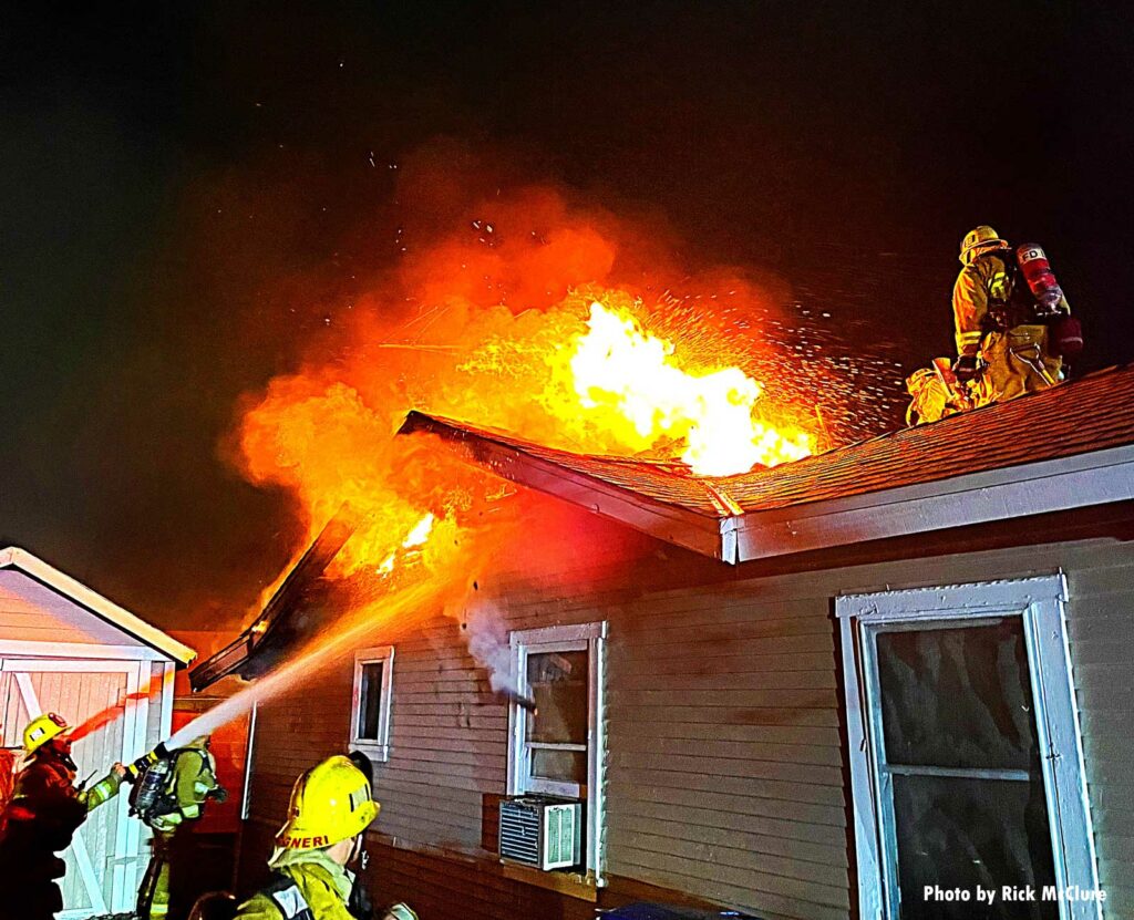 Flames tear through the roof of a home as LAFD members operate