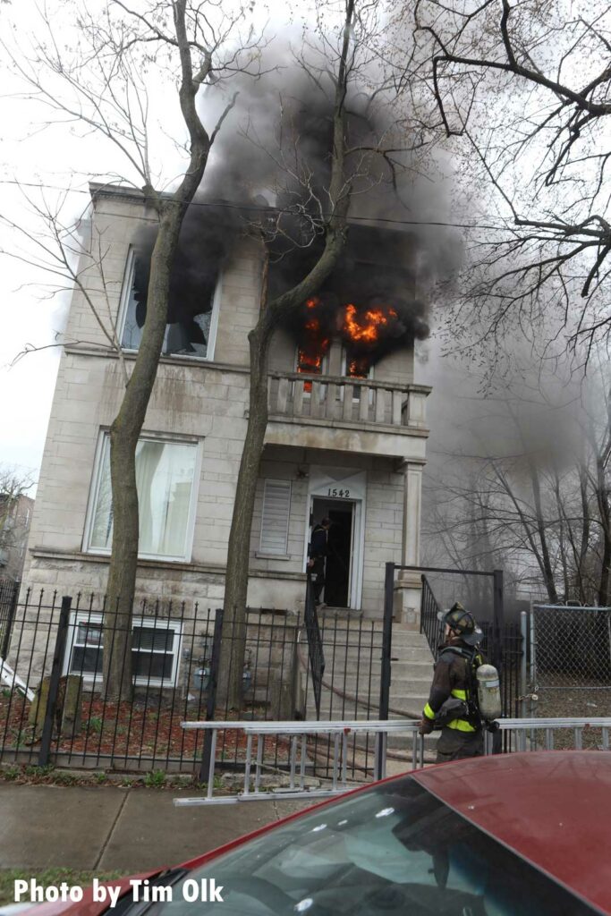 A Chicago firefighter carries a ladder to a building with flames showing from the windows