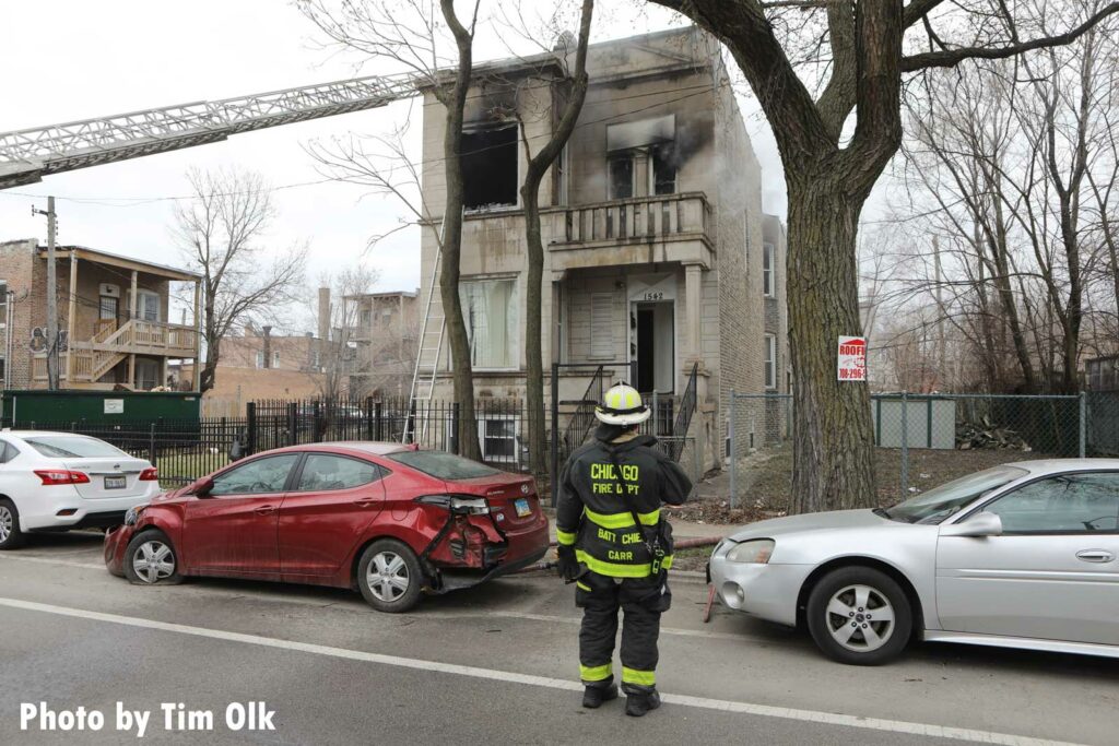 An aerial ladder raised to the roof of the building with a Chicago Fire Department battalion chief looking on