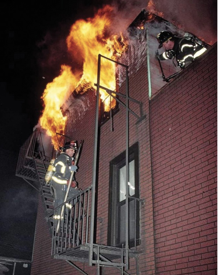 The roof firefighter recons the conditions in the rear while the outside vent firefighter operates from the fire escape below.