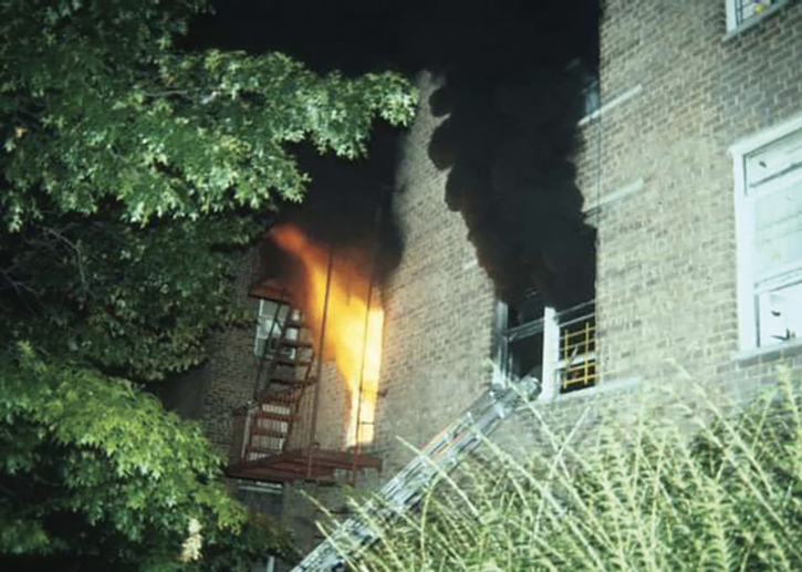 Heavy fire and thick, black smoke vent from the windows, indicating advanced and rapidly deteriorating conditions.