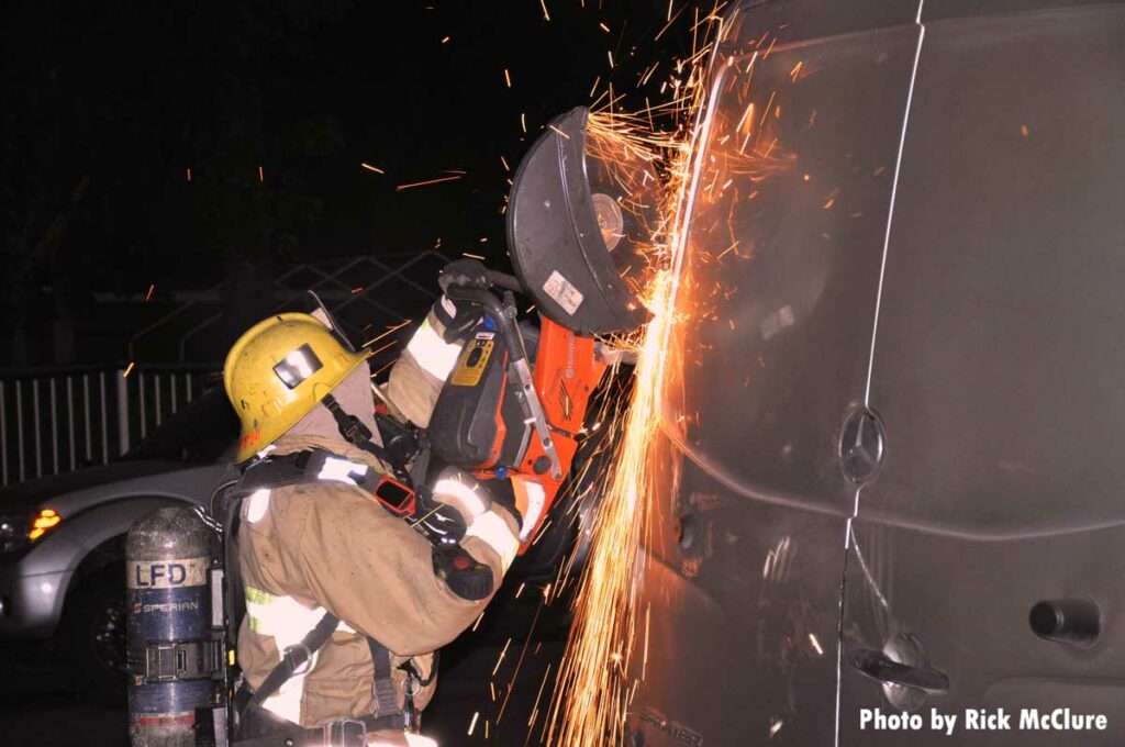 Firefighter using a circular saw to cut the rear door of a burning van