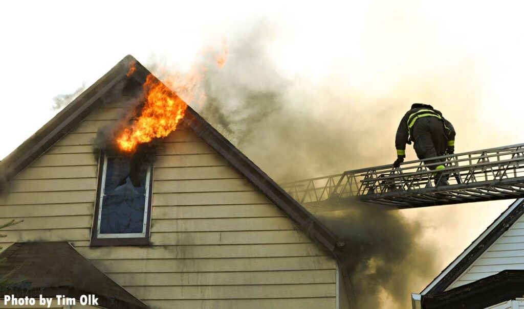 Flames shoot from above a window as a firefighter climbs a Chicago aerial ladder