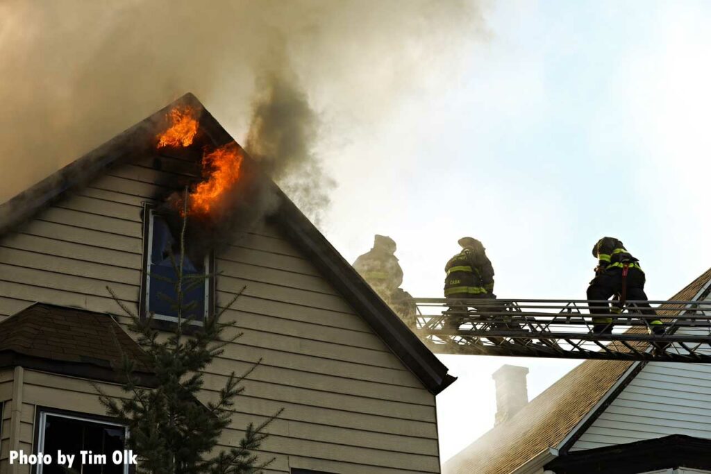 Flames shoot from the roofline as Chicago firefighter operate on aerial ladder