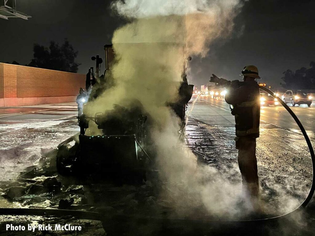 Firefighter with a hoseline standing near burnt tractor trailer