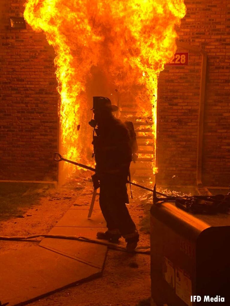 Flames roar from a doorway with an Indianapolis firefighter in front of it