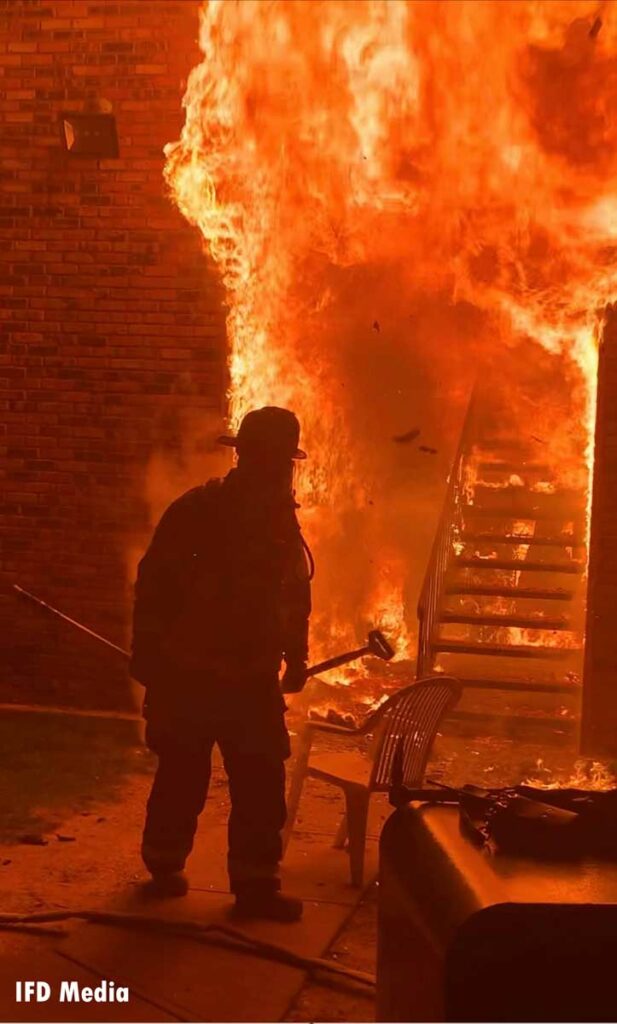 Firefighter with a hook with raging flames behind him