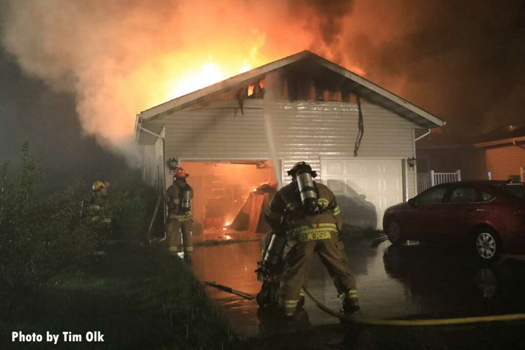 Firefighters put water onto garage area as flames burn through roof of home