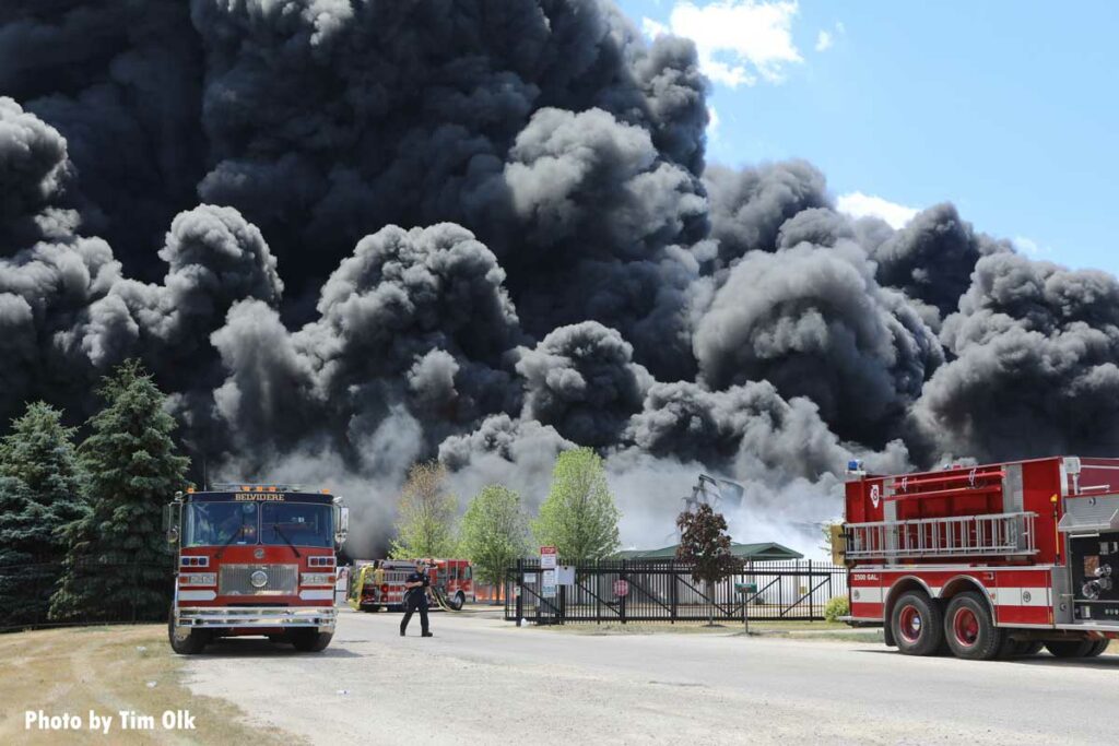 Huge plumes of black smoke drift past multiple fire apparatus